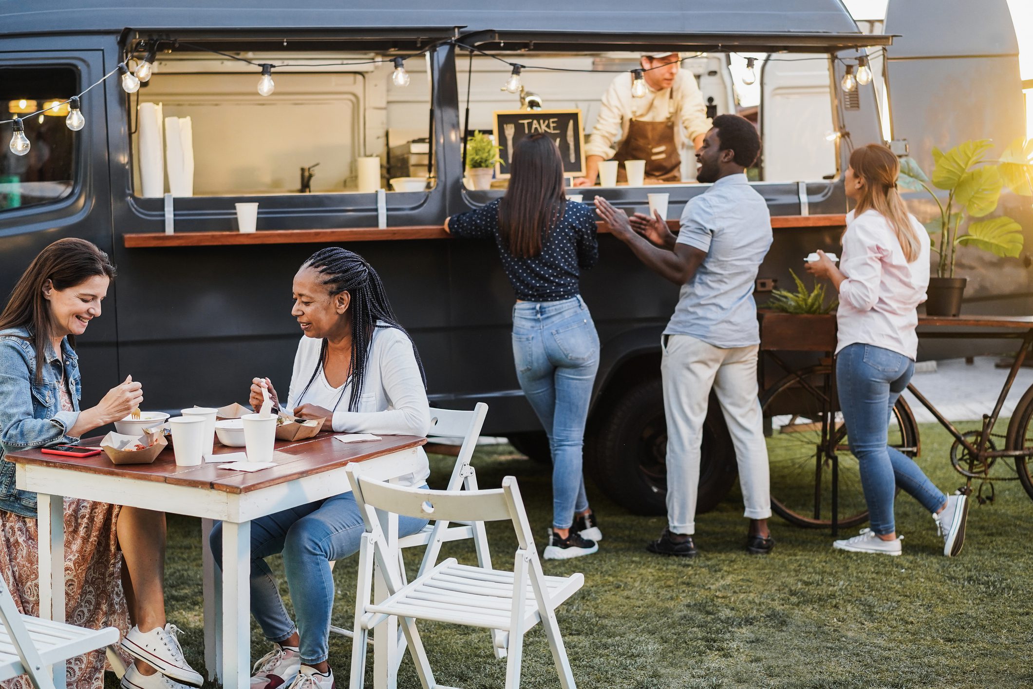 People ordering food from a food truck while others sit and eat outside.