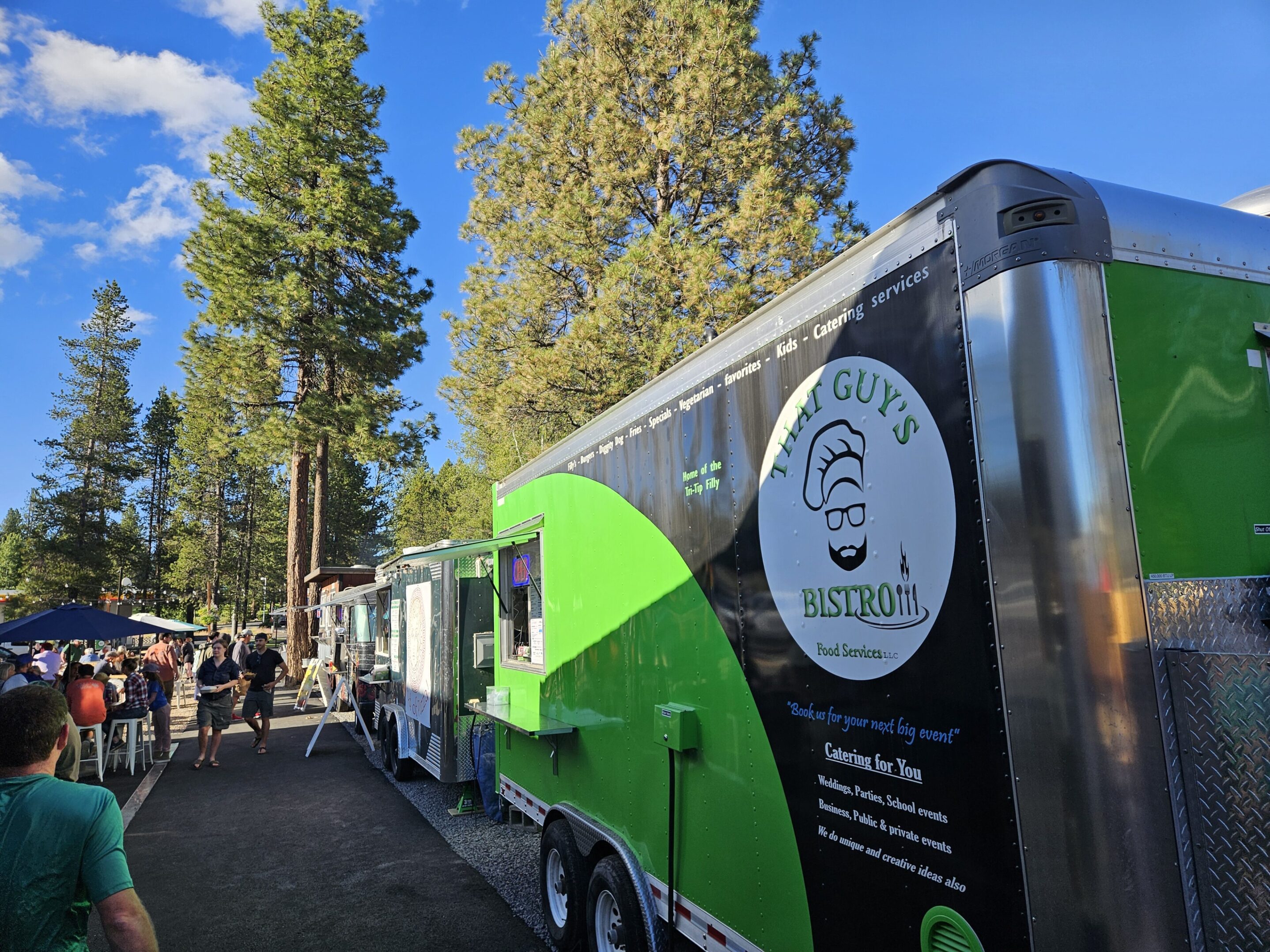Food trucks lined up outdoors under tall trees on a sunny day.