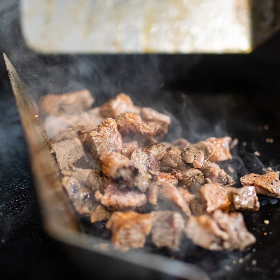 Grilled meat pieces cooking on a hot grill with smoke rising.