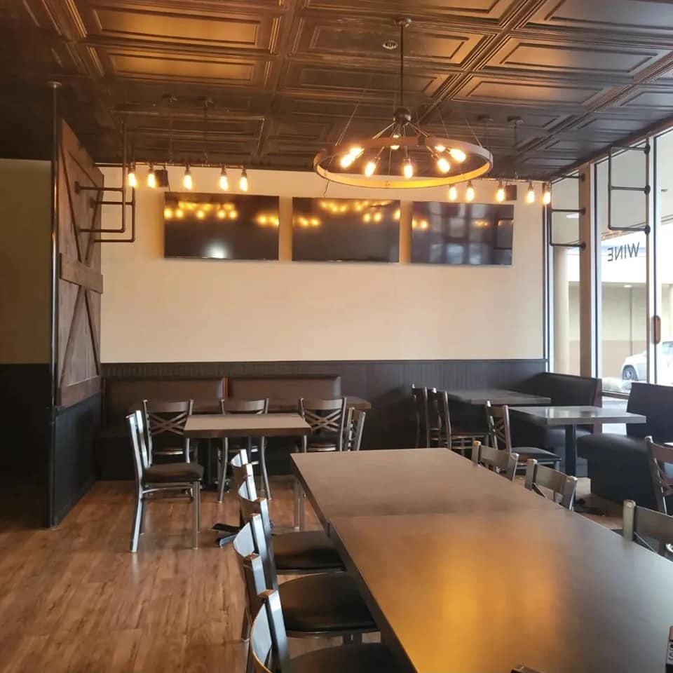 Cozy restaurant interior with wooden tables, black chairs, and warm lighting.